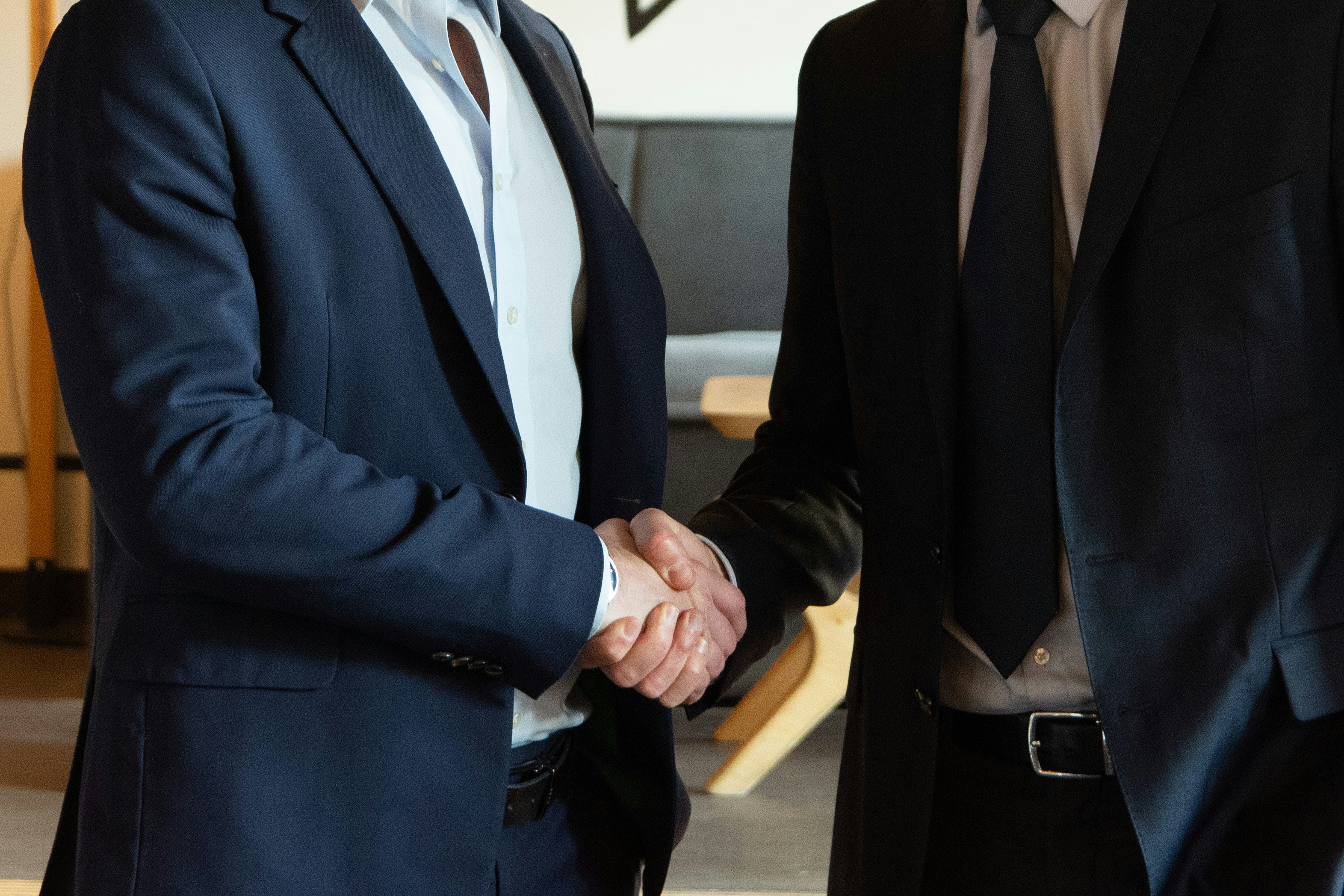 Two business professionals shaking hands in dark suits.